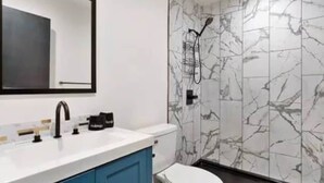 A modern bathroom with a white sink, blue cabinets, a toilet, and a shower with a marble wall. - Blue&Gold Art Deco 2BR1BA Loft close to Genentech (South San Francisco)