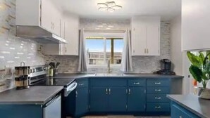 A modern kitchen with dark blue cabinets, a black countertop, and a large window providing natural light. - Blue&Gold Art Deco 2BR1BA Loft close to Genentech (South San Francisco)