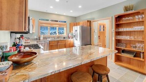 A kitchen with wooden cabinets, a marble countertop, a stainless steel refrigerator, and a glass display shelf. - Tempest Ridge Townhouse 34 (Newry)