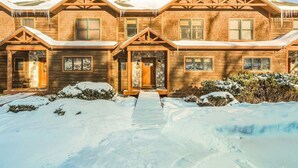 A wooden cabin with a stone fireplace, a covered entryway, and a snow-covered landscape. - Tempest Ridge Townhouse 34 (Newry)