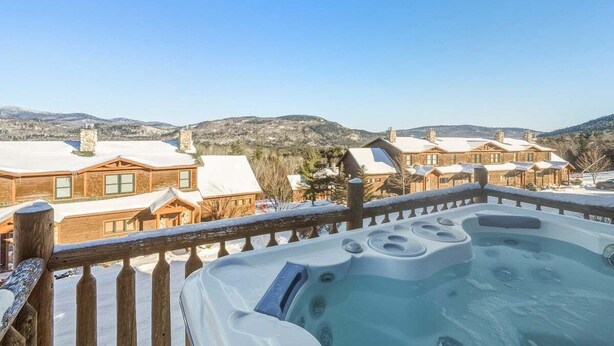 A hot tub on a balcony overlooking a snowy landscape with wooden buildings. - Tempest Ridge Townhouse 34 (Newry)