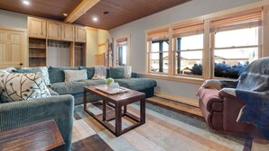 A cozy living room with a sofa, armchair, and coffee table, wooden cabinets, and large windows. - Tempest Ridge Townhouse 34 (Newry)