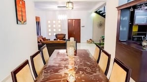 A dining area with a long table, chairs, a ceiling fan, and a kitchen area visible to the right. - Ravo Residence (Galle)
