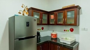 A compact kitchen with a stainless steel refrigerator, wooden cabinets, and a black countertop. - Ravo Residence (Galle)