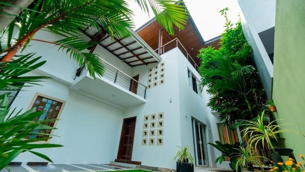 A modern two-story house with a balcony, surrounded by lush greenery and a well-maintained lawn. - Ravo Residence (Galle)