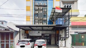 Un edificio commerciale con ingresso coperto, due auto parcheggiate e condizionatori d'aria sulla facciata.