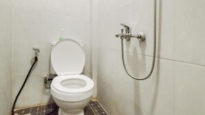Un bagno piccolo rivestito di piastrelle, con un water bianco, un soffione e un tubo a vista.