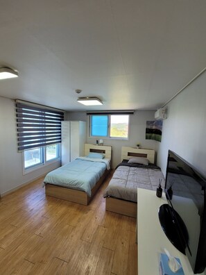 A bedroom with two beds, a desk, a chair, and a window with blinds. - Incheon Airport ANN Guesthouse (Incheon)