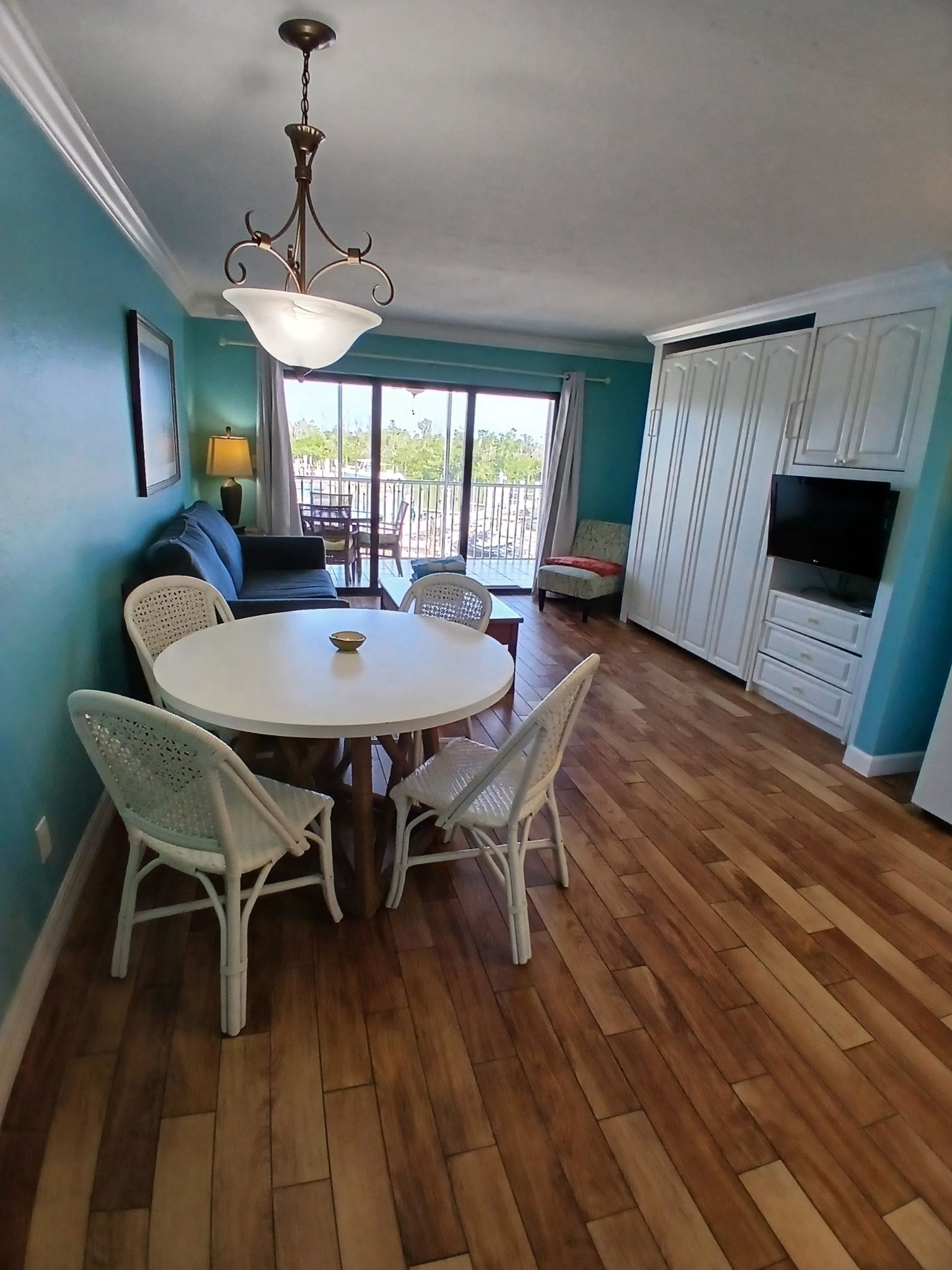 A dining area with a round table and four chairs, a sofa, a TV, and a balcony with a view.