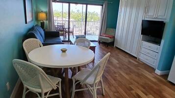 A dining area with a round table and four chairs, a sofa, a TV, and a balcony with a view.