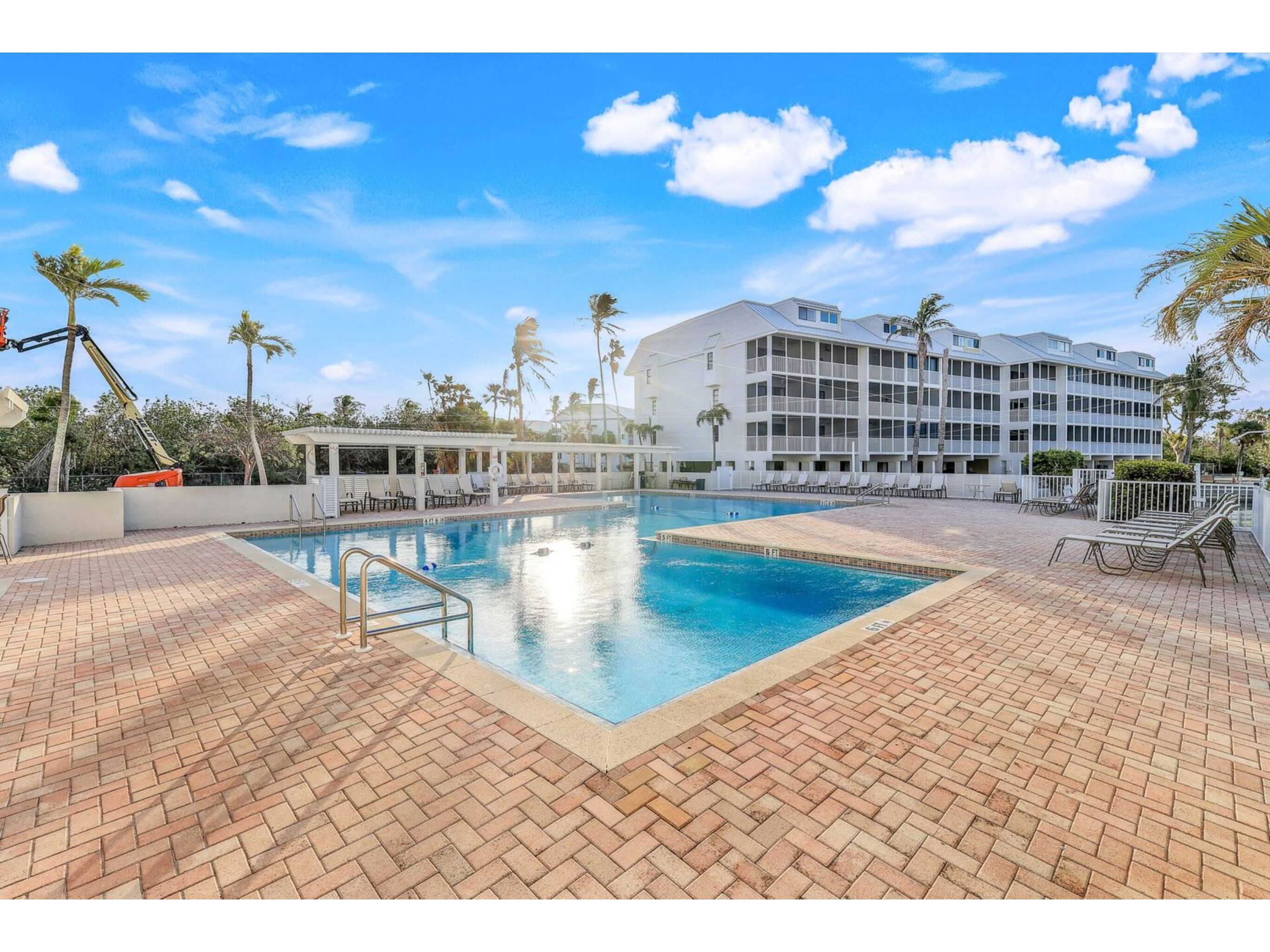 A swimming pool with a brick deck, surrounded by lounge chairs and palm trees.