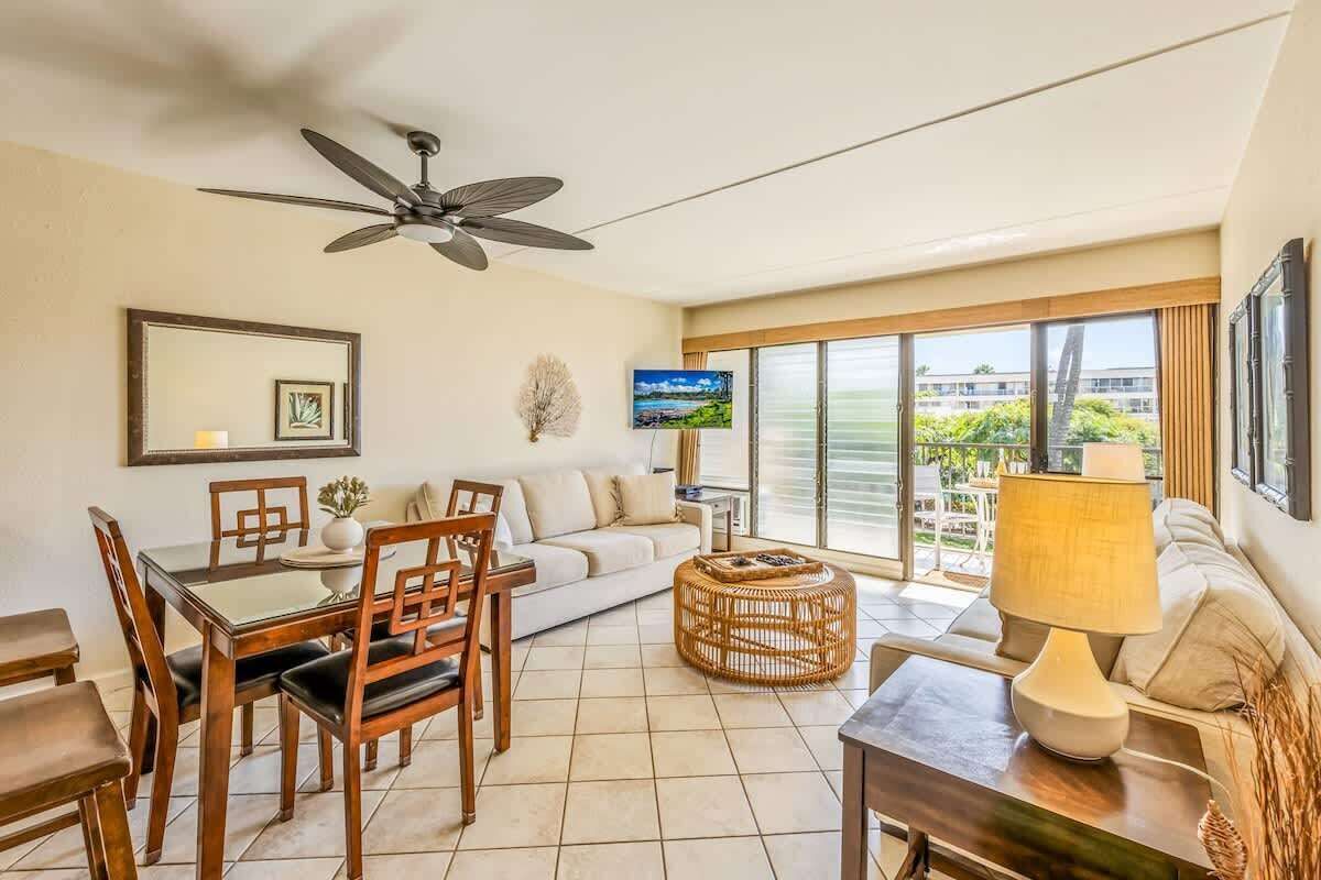 A modern living room with a dining area, a ceiling fan, a TV, and large windows offering a view of the outdoors.