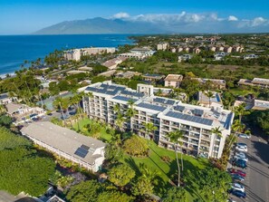 A hotel with multiple floors, solar panels on the roof, and a view of the ocean. - Partial oceanview 1 bedroom condo, AC, across from beach, near shops & dining (Kihei)