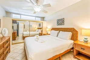 A hotel room with a bed, bedside tables, a ceiling fan, a mirror, and a wardrobe. - Partial oceanview 1 bedroom condo, AC, across from beach, near shops & dining (Kihei)