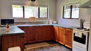 A modern kitchen with wooden cabinets, a built-in oven, a microwave, and a window with a view of greenery. - Paradise At The Beach (Coromandel)
