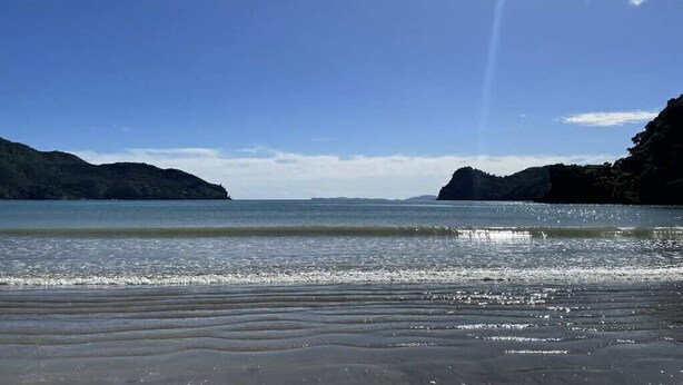 A beach with a clear sky, calm sea, and distant mountains. - Paradise At The Beach (Coromandel)