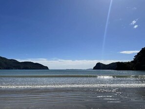 A beach with a clear sky, calm sea, and distant mountains. - Paradise At The Beach (Coromandel)