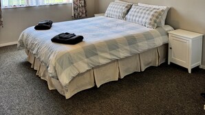 A bedroom with a large bed, a nightstand, a window with curtains, and a ceiling light. - Paradise At The Beach (Coromandel)