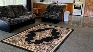 A spacious living room with a large black and beige rug, two dark sofas, and a kitchen in the background. - Paradise At The Beach (Coromandel)