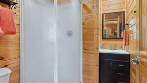 Un baño de cabaña de madera con una puerta de ducha blanca, un lavabo con espejo y un inodoro.