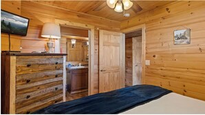 Una habitación de cabaña de madera con una cama, un televisor, una lámpara y una puerta que da a una cocina.