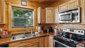 Una cocina con armarios de madera, un lavamanos de acero inoxidable, un microondas y una estufa.