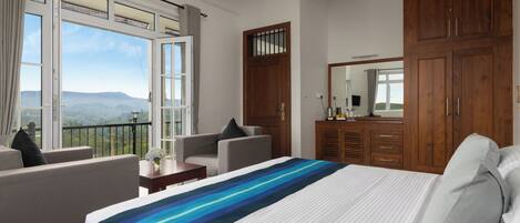 Habitación de hotel con una cama grande, un sofá, un escritorio y un armario. Tiene un balcón con vistas a las montañas.
