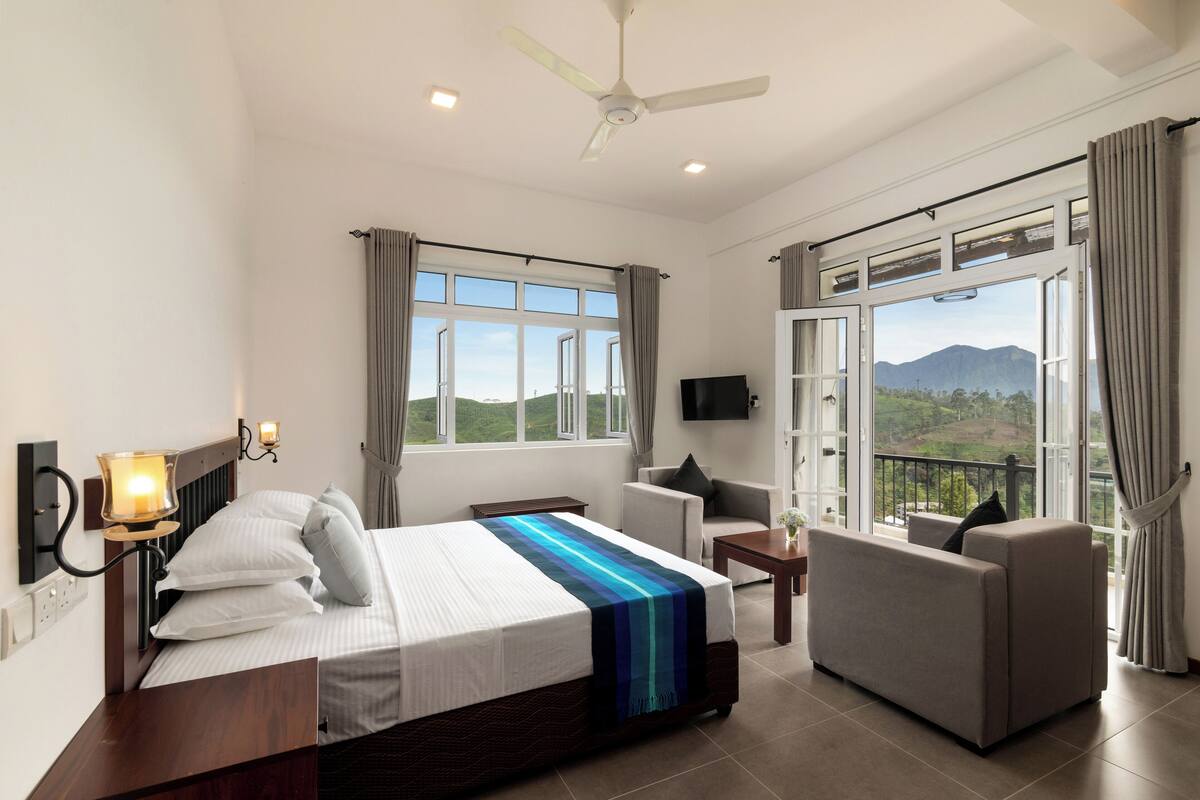 Ein Hotelzimmer mit Bett, Sofa, Fernseher und großen Fenstern mit Blick auf die Berge.