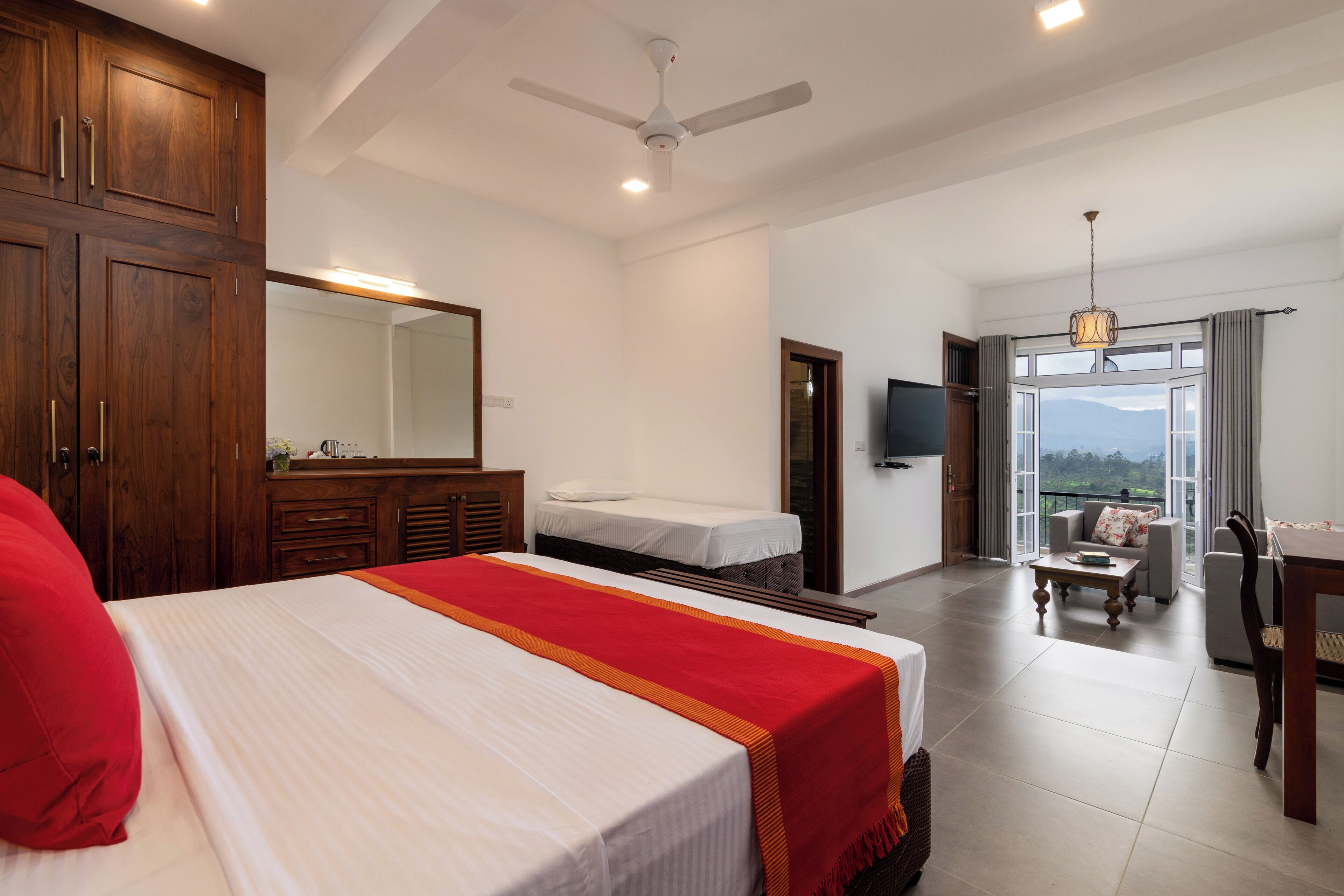 A hotel room with a large bed, a desk, a chair, a sofa, a TV, and a balcony with a view.