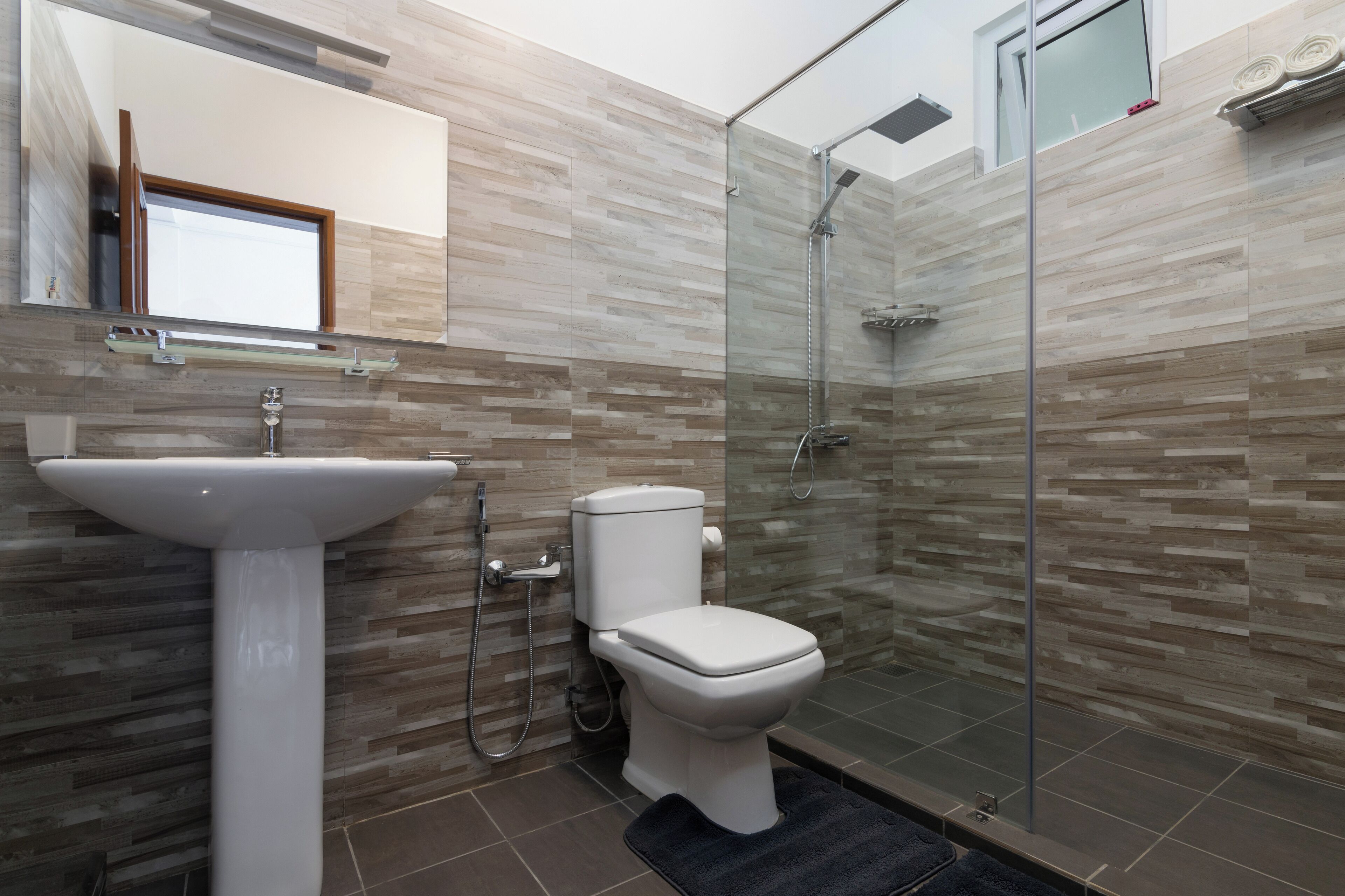 A modern bathroom with a pedestal sink, toilet, and glass-enclosed shower.