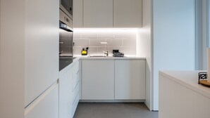 Ett modernt kök med vita skåp, en inbyggd ugn och en diskho i rostfritt stål.