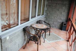 A small outdoor seating area with two wicker chairs and a round table, a window with curtains, and a brick wall. - TAU-House (Almaty)