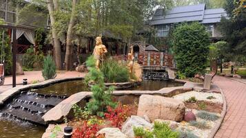 Un jardin agrémenté d’un bassin, de statues et d’un bâtiment doté d’un toit traditionnel.