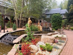 Un jardín con un estanque, estatuas y un edificio con tejado tradicional.