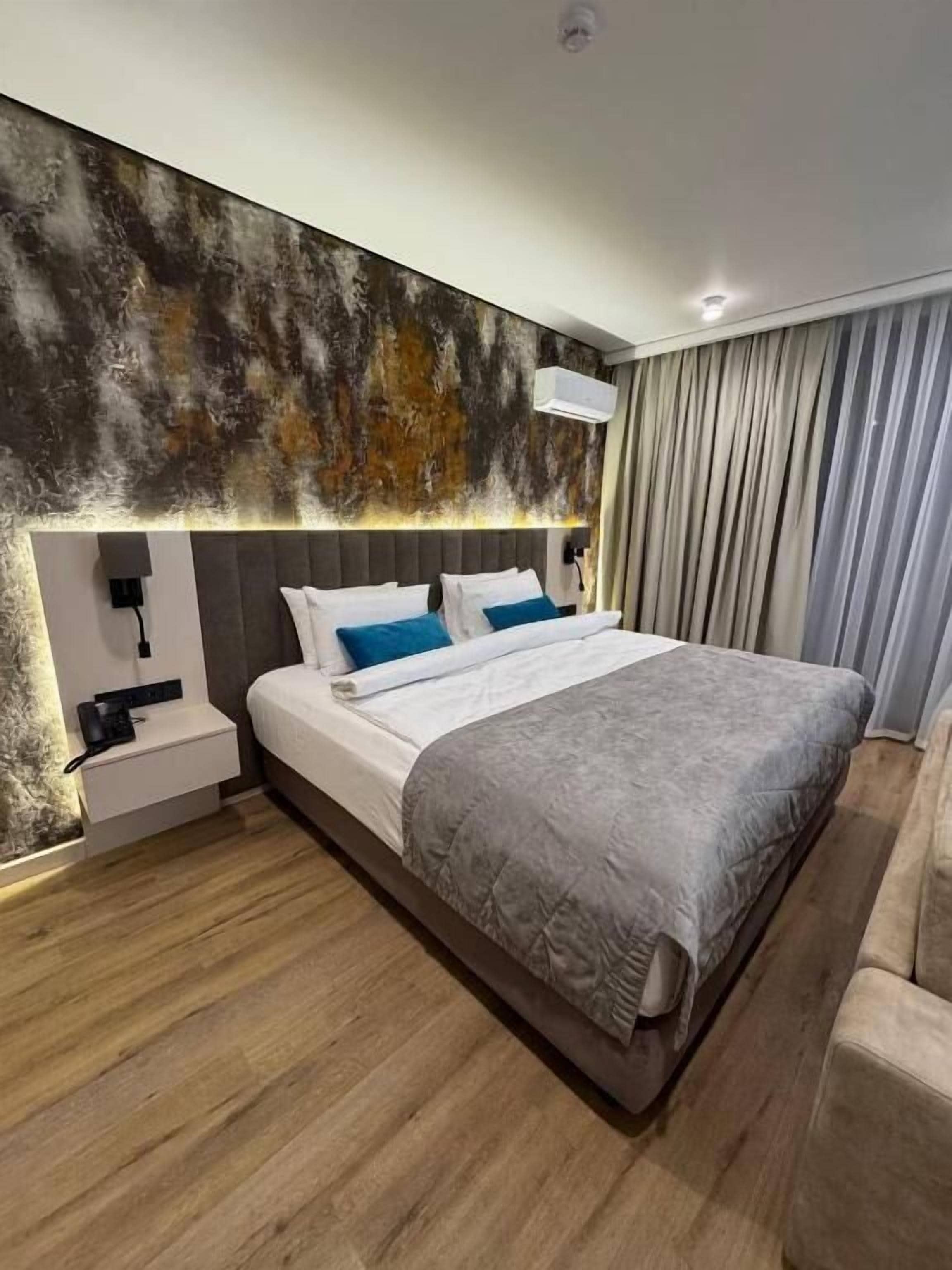 A modern hotel room with a large bed, a bedside table, and a wall-mounted air conditioning unit.