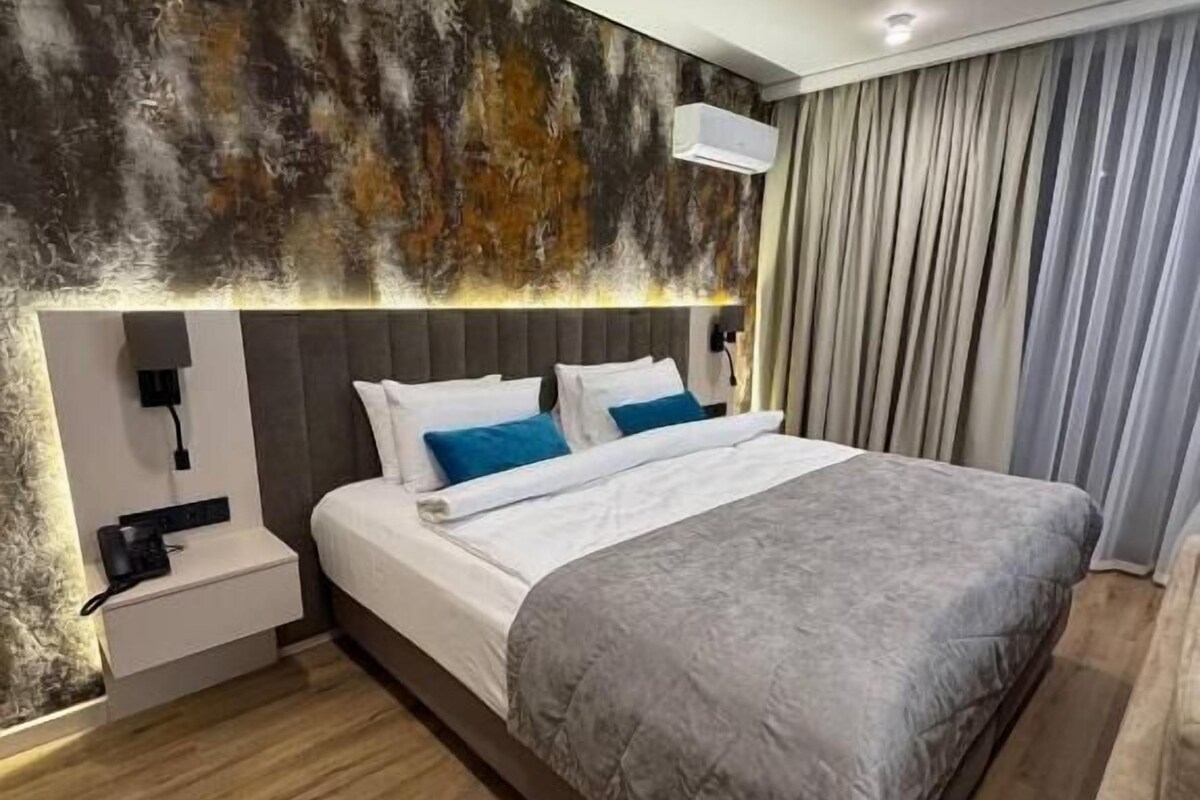 A modern hotel room with a large bed, a bedside table, and a wall-mounted air conditioning unit.