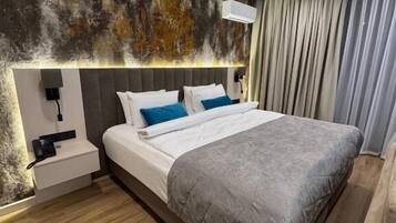 A modern hotel room with a large bed, a bedside table, and a wall-mounted air conditioning unit.