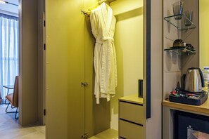 A hotel room with a yellow door, a robe hanging on the door, a minibar, and a seating area with a chair. - TAU-House (Almaty)