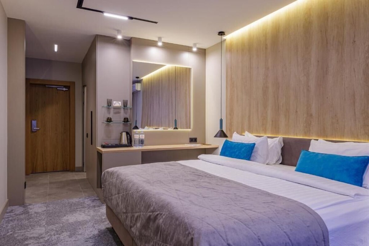 A modern hotel room with a large bed, a bedside table, a mirror, and a wooden headboard.