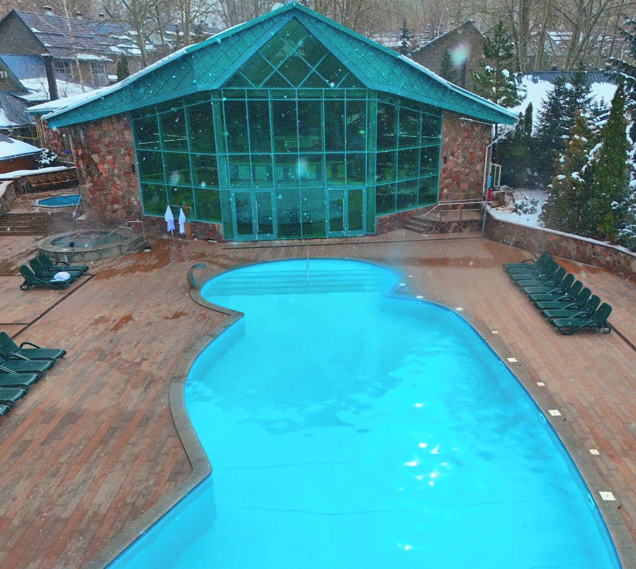 A swimming pool with a unique shape, surrounded by lounge chairs and a stone building with a glass facade.