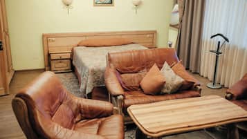 Una habitación con una cama, una mesita de noche de madera, un sofá de cuero con cojines y una mesa de centro de madera.