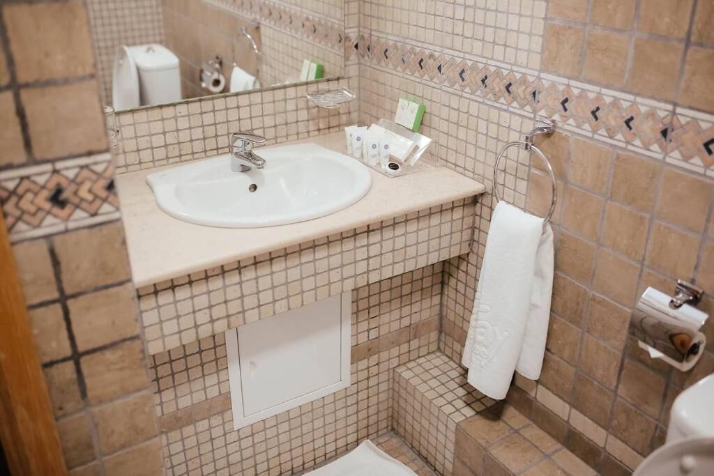 A bathroom with a sink, mirror, towel rack, and toiletries.