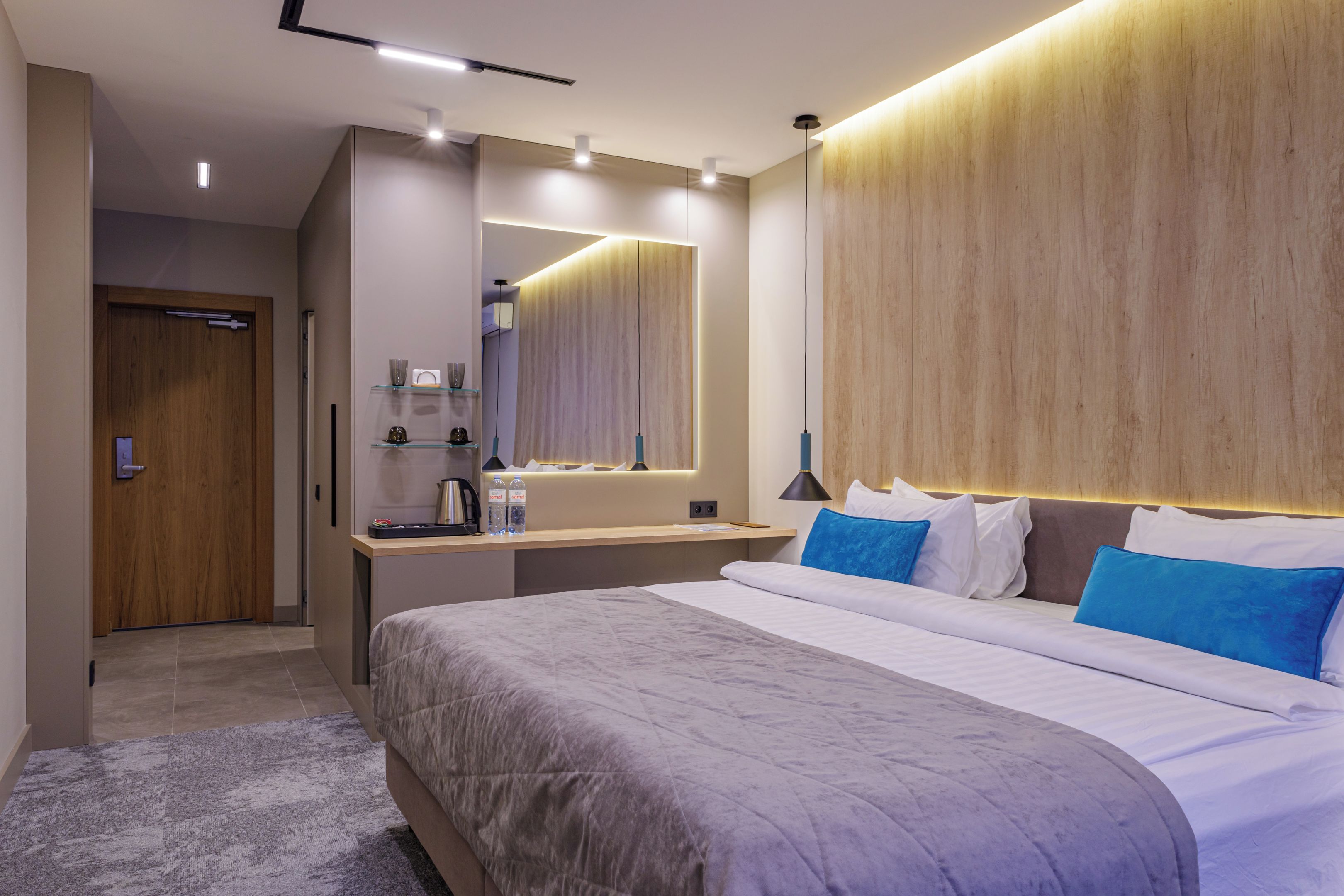 Una habitación de hotel moderna con una cama grande, una mesita de noche, un espejo y un cabecero de madera.