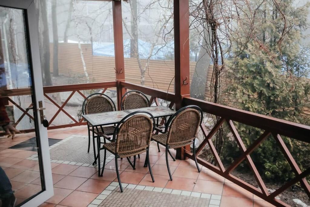 A covered patio with a table and chairs, a view of trees and a wooden deck in the background.