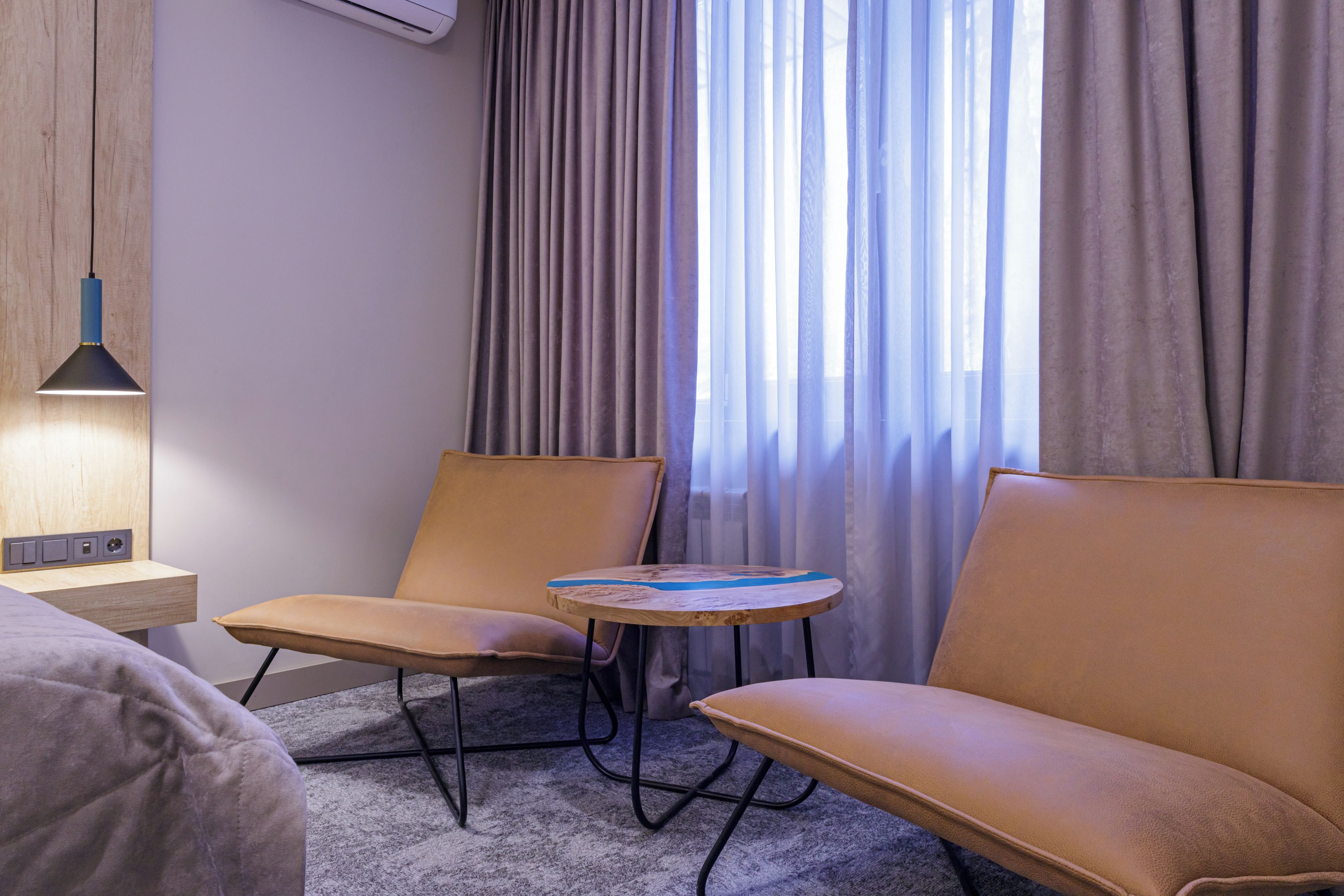 A hotel room with a bed, two armchairs, a small round table, a lamp, and a window with curtains.