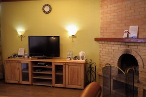Una sala de estar con televisor de pantalla plana, mueble bajo de madera, dos lámparas de pared, chimenea de ladrillo y un reloj en la pared.