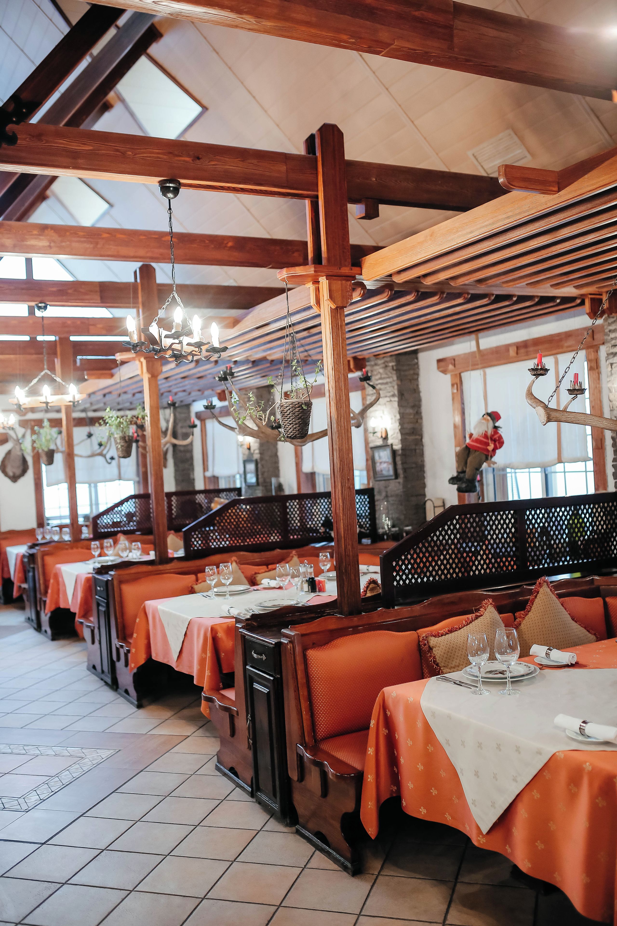 Interior de restaurante con vigas de madera, plantas colgantes y mesas preparadas para comer.