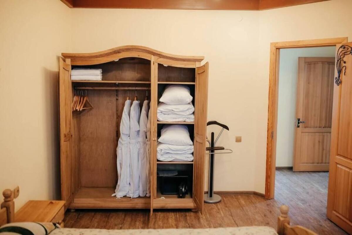 A wooden wardrobe with multiple shelves, a hanging rack, and a small table with a lamp.