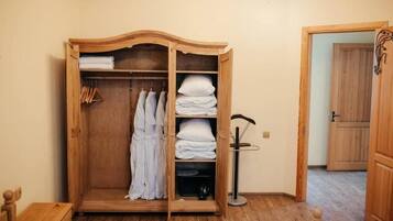 Une armoire en bois avec plusieurs étagères, une tringle pour suspendre les vêtements et une petite table avec une lampe.