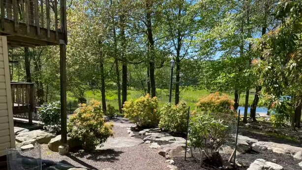 A garden pathway with rocks and shrubs, a wooden deck, and a view of a lake.